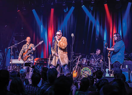 A man wearing a fur coat is singing into a microphone on stage in front of a crowd. AI generated content