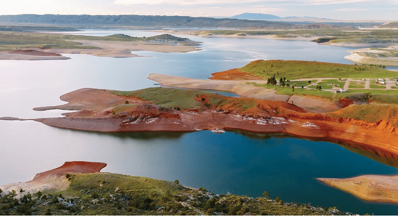 A large body of water with a red shore and a mountain in the background. AI generated content